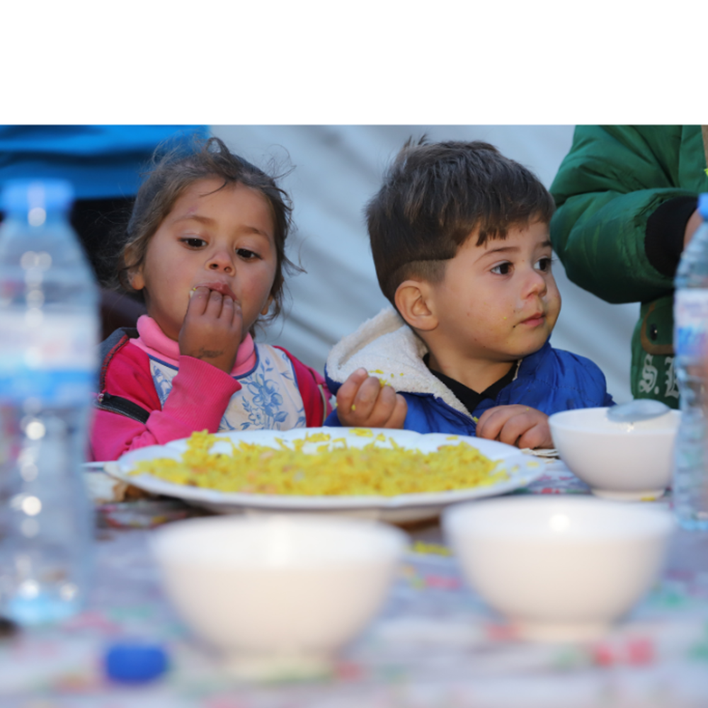 young children eating with a plate of food in font of them
